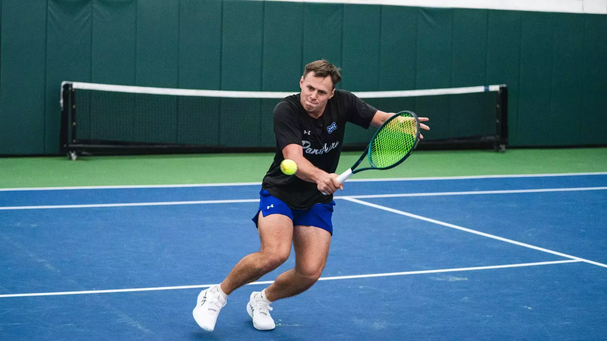 Cem driving through a backhand on an indoor court